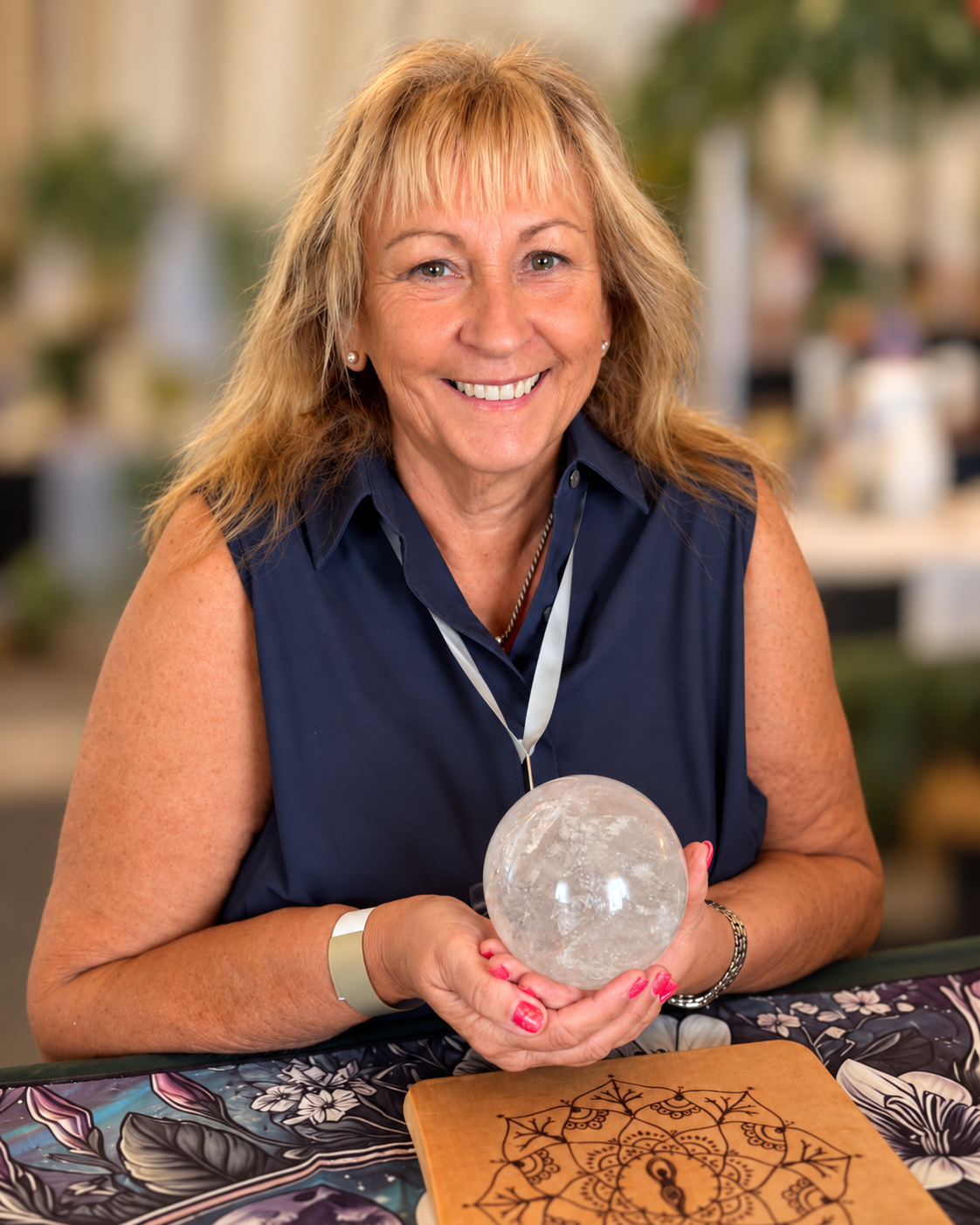 Liz Roberts smiling and holding a clear crystal sphere, with a softly blurred background.